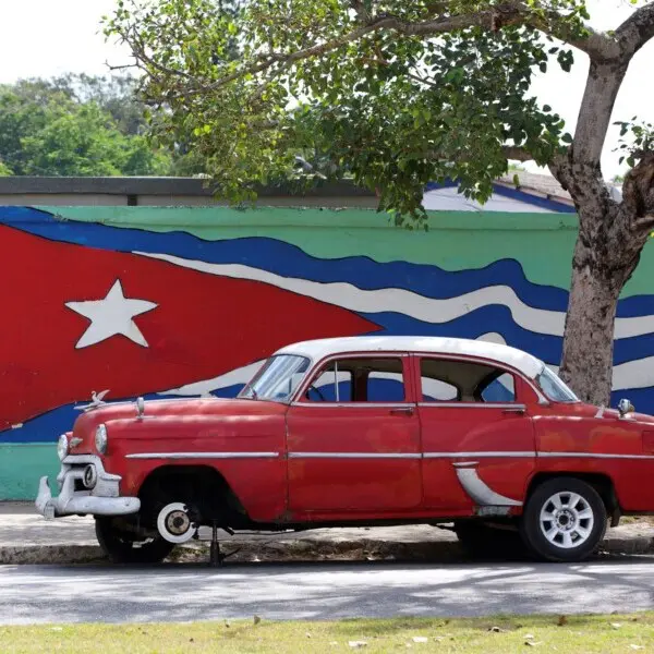 Kuba, rotes Oldtimer Auto vor einer Mauer mit Kuba-Flagge, Latin America Tours, Reisen